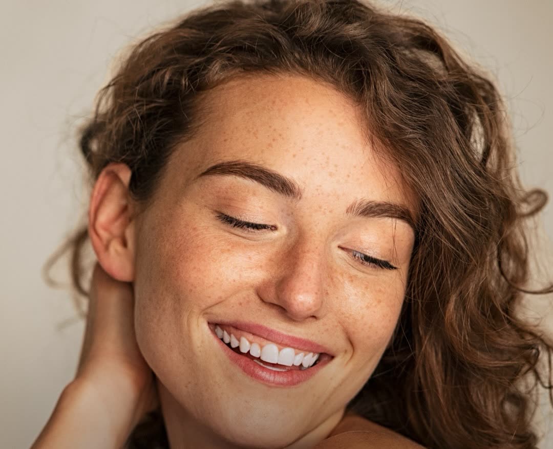 Mulher sorrindo de olhos fechados, pele real com sardas, em luz quente